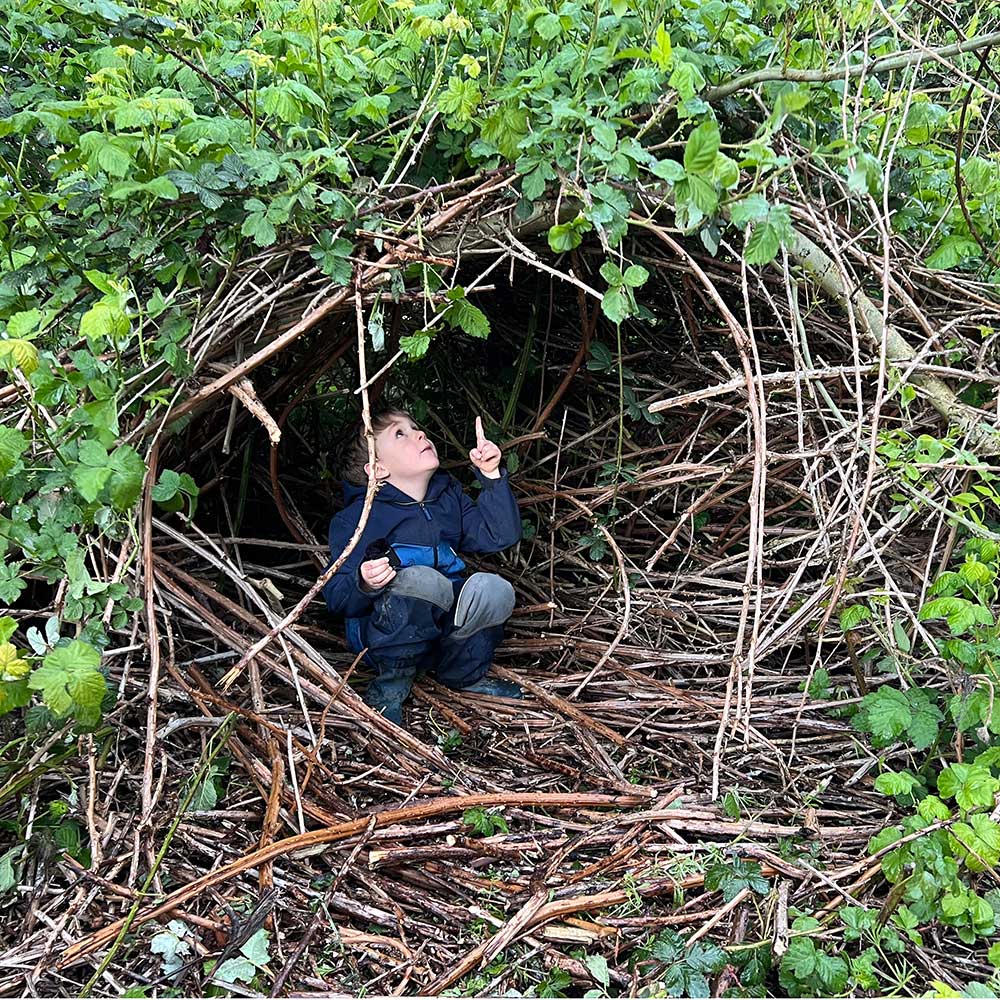 Ein Junge sitzt begeistert in einer wild wuchernden Brombeerhöhle