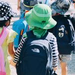 Eine Gruppe von Schulkindern von hinten fotografiert mit Ranzen auf dem Rücken Hand in Hand unterwegs
