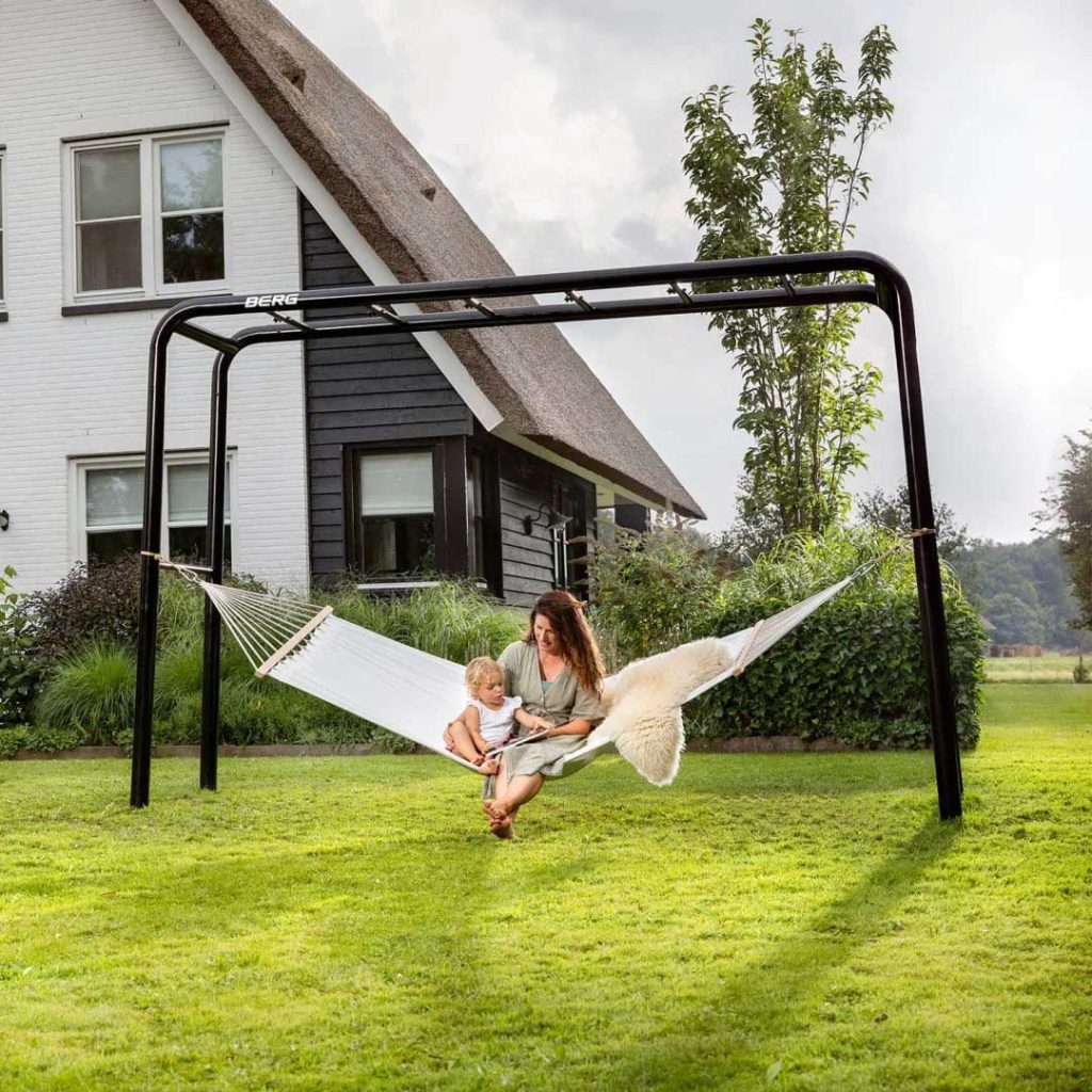 Eine junge Frau mit Baby im Schoß chillt im Garten in einer Hängematte, die an einem Klettergerät befestig ist.