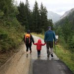 Eltern gehen mit ihrem Kind in der Mitte Hand in Hand einen Feldweg entlang